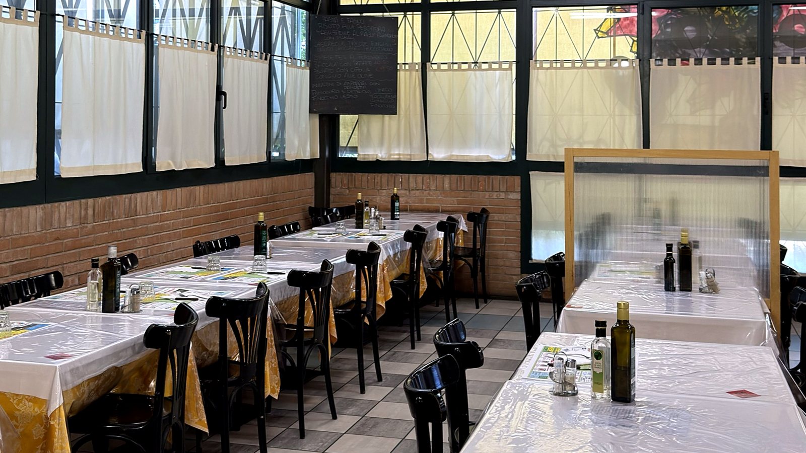 La sala apparecchiata, con le tovaglie bianche e gialle e le bottiglie d'olio sul tavolo